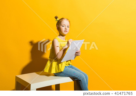 Girl with red hair on a yellow background. Beautiful girl is sitting on the table and is holding a Girl with red hair on a yellow background. Beautiful girl is sitting on the table and is holding a 41471765