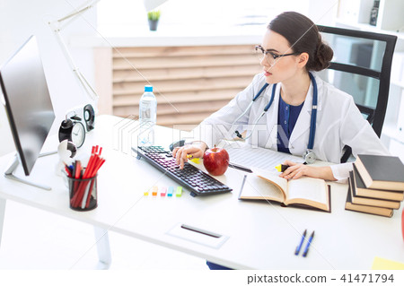 A beautiful young girl in a white robe sits at a table, holds a marker and a pen in her hand and 41471794