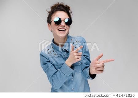 Young brunette girl in round glasses. Hairs are gathered in a bun. The girl points with her fingers. 41471826