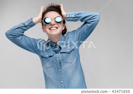 Young brunette girl in round glasses. Hairs are gathered in a bun. The girl holds her hands behind 41471850
