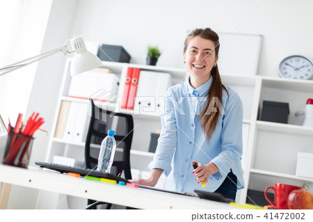 A young girl in the office is standing near the table and holding a yellow marker in her hand. 41472002
