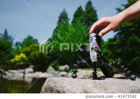 Photograph male hand handling an old vintage camera on tripod in front of water pond in Planten un Photograph male hand handling an old vintage camera on tripod in front of water pond in Planten un 41473582