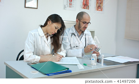 Male doctor counting money and giving it to his female partner Male doctor counting money and giving it to his female partner 41497206