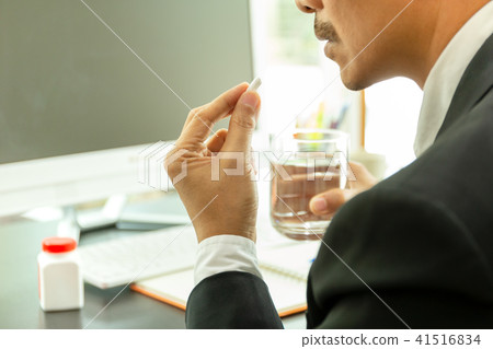 Businessman taking pills at work desk in office Businessman taking pills at work desk in office 41516834