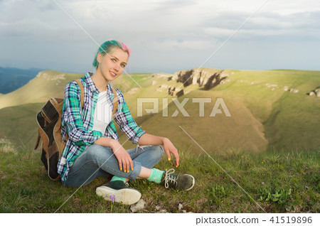 Portrait of young smiling woman traveler with multi-colored hair. Sitting high in the mountains in Portrait of young smiling woman traveler with multi-colored hair. Sitting high in the mountains in 41519896