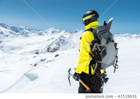 A mountaineer man holds an ice ax high in the mountains covered with snow. View from the back 41519938