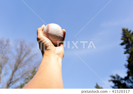 Hand holding baseball against blue clean sky Hand holding baseball against blue clean sky 41520317