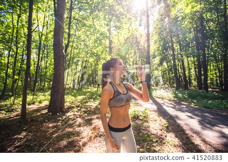 Young woman drinking water after running outdoors Young woman drinking water after running outdoors 41520883