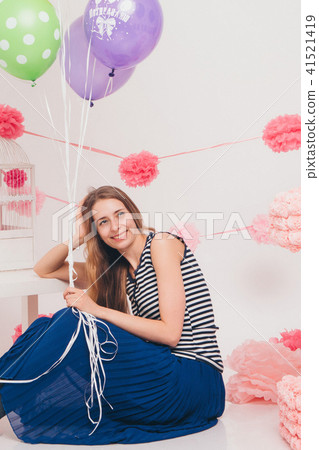 the blonde smiles and looks at the camera between the colored balls on a white background. Studio the blonde smiles and looks at the camera between the colored balls on a white background. Studio 41521419