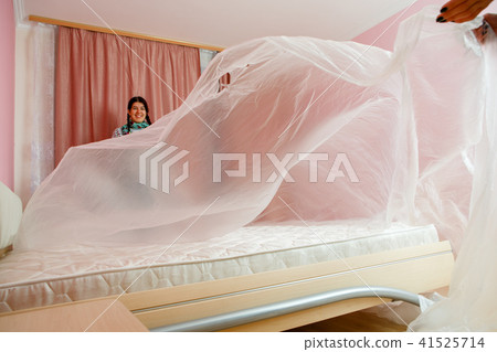 Image of young woman covering bed with polyethylene Image of young woman covering bed with polyethylene 41525714