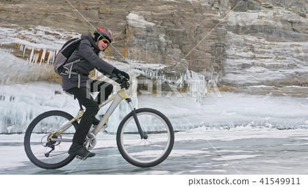 Man is riding bicycle near the ice grotto. The rock with ice caves and icicles is very beautiful 41549911