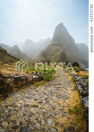 Aranhas mountain peak in the valley with house ruins and stony hiking path going up the mountain Aranhas mountain peak in the valley with house ruins and stony hiking path going up the mountain 41553730