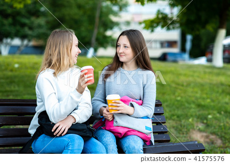 Two teenage girls are schoolgirls. In summer in the park on the street. Holds hands with cups of 41575576