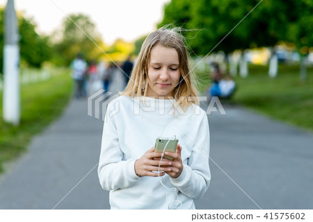 A teenage girl. In the summer in city. In his hands holds a smartphone. Listens to music watching 41575602