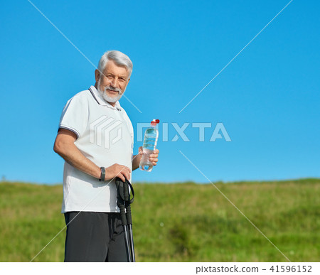 Old man keeping water bottle and tracking sticks. Old man keeping water bottle and tracking sticks. 41596152
