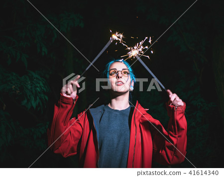 Portrait of hipster girl with blue dyed hair with sparklers in hands and reflection of it in glasses Portrait of hipster girl with blue dyed hair with sparklers in hands and reflection of it in glasses 41614340
