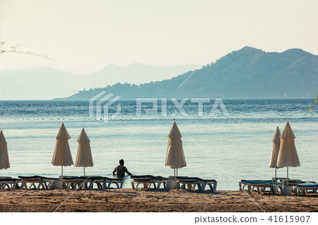White umbrellas, blue sea big mountains on horizon White umbrellas, blue sea big mountains on horizon 41615907