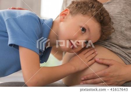 Curious dark-eyed boy putting his ear to pregnant tummy 41617643