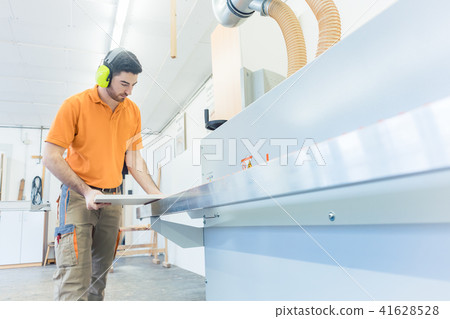 Carpenter in furniture factory working on veneer machine Carpenter in furniture factory working on veneer machine 41628528