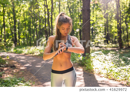 Young athlete woman checking fitness progress on her smart watch. Female runner using fitness app to 41629972