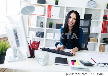 A young girl is sitting at the office at the table and typing text on the keyboard. 41635063