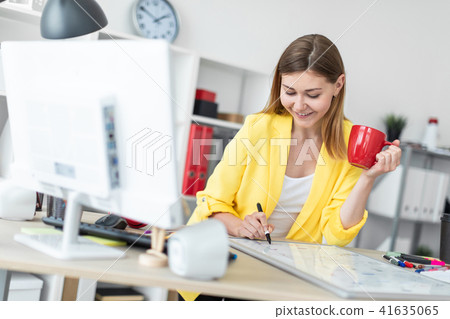 A young girl stands near a table and holds a red cup and a marker in her hands. Before the girl on 41635065