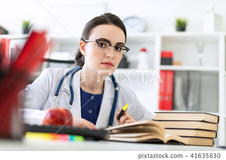 A beautiful young girl in a white robe is sitting at the computer desk with a marker and a book. A 41635830
