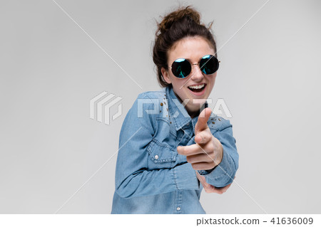 Young brunette girl in round glasses. Hairs are gathered in a bun. The girl points with her fingers. 41636009