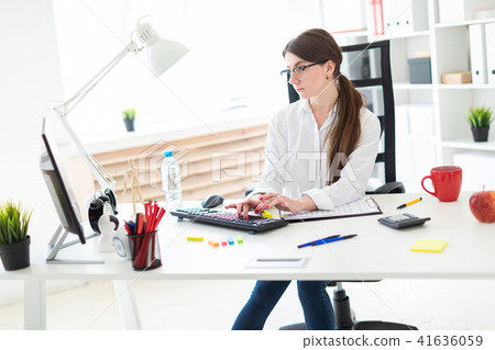 A young girl is sitting at a table in the office and typing on the keyboard. A young girl is sitting at a table in the office and typing on the keyboard. 41636059