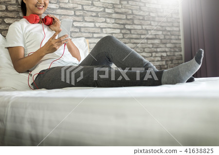 Young woman sitting in her bed and listening music in her bedroo Young woman sitting in her bed and listening music in her bedroo 41638825