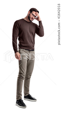A fashionable man in glasses and casual clothes stands touching his head with one hand in doubt. 41642018