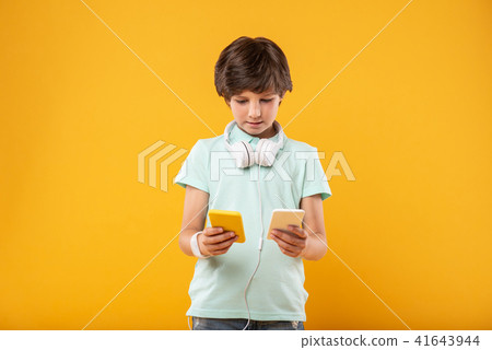 Concentrated schoolboy holding two phones 41643944