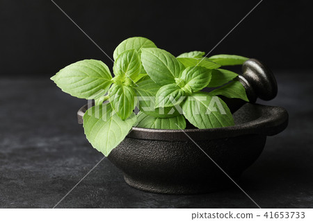 Fresh green basil leaves in cast iron mortar on Stock Photo