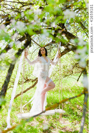 Seductive young bride in white negligee and lingerie standing on a white swing 41659181