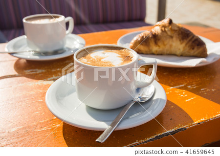 Two cups of invigorating cappuccino and a croissant for breakfast Two cups of invigorating cappuccino and a croissant for breakfast 41659645