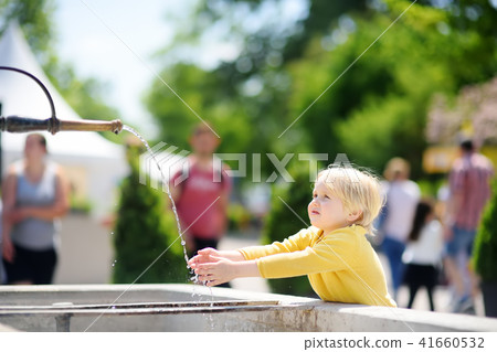 Little blonde hair boy playing with city fountain on sunny summer day 41660532