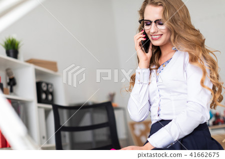 A beautiful young girl sat down on the table in the office and was talking on the phone. Before the A beautiful young girl sat down on the table in the office and was talking on the phone. Before the 41662675