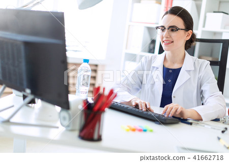 A beautiful young girl in a white robe is sitting at the table and typing on the keyboard. 41662718