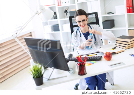 A beautiful young girl in a white robe sits at a computer desk, holds a marker in her hand and opens 41662720