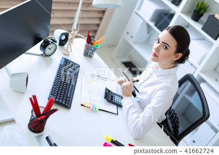 A young girl in the office sits at a table, holds a marker and a pencil in her hand and works with a 41662724