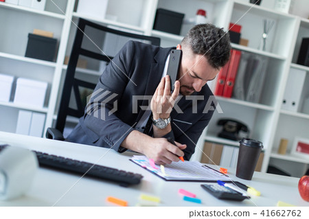 A man is sitting at the desk at the office, talking on the phone and writing a marker in the 41662762