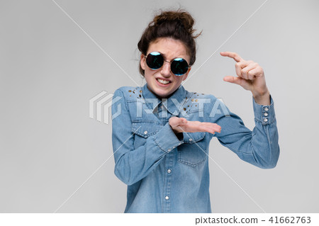 Young brunette girl in round glasses. Hairs are gathered in a bun. Girl shows thumbs up size. 41662763