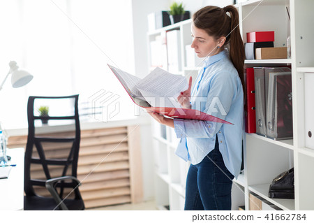A young girl in the office is standing near the shelter and scrolls through the folder with the 41662784