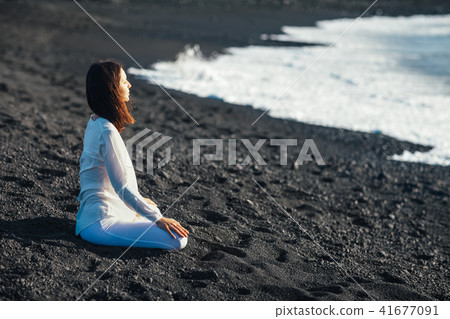woman meditating in Lotus Pose in black sand beach 41677091