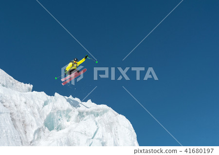 A jumping skier jumping from a glacier against a blue sky high in the mountains. Professional skiing A jumping skier jumping from a glacier against a blue sky high in the mountains. Professional skiing 41680197