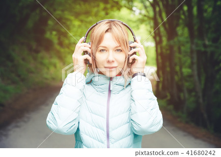 Portrait of a beautiful young woman holding headphones listening to music outdoors in the forest Portrait of a beautiful young woman holding headphones listening to music outdoors in the forest 41680242