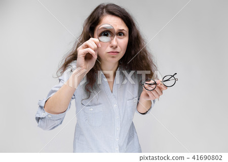 Young brunette girl with glasses. A girl looks through a magnifying glass. Young brunette girl with glasses. A girl looks through a magnifying glass. 41690802