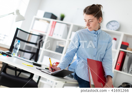 A young girl in the office is standing, leaning on a table, and writing in a diary. 41691266
