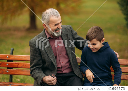 Grandpa and his grandson spend time together in the park. They are sitting on the bench. Walking in Grandpa and his grandson spend time together in the park. They are sitting on the bench. Walking in 41696573