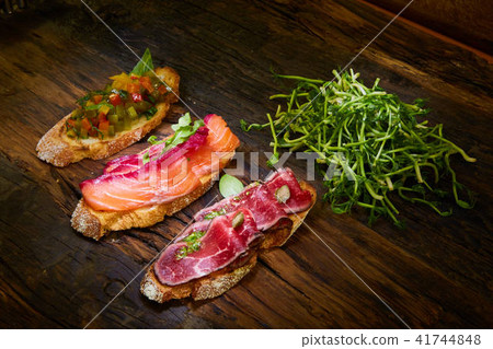 Assorted bruschetta with roast beef, vegetables and lightly salted salmon with greens leaves on Assorted bruschetta with roast beef, vegetables and lightly salted salmon with greens leaves on 41744848
